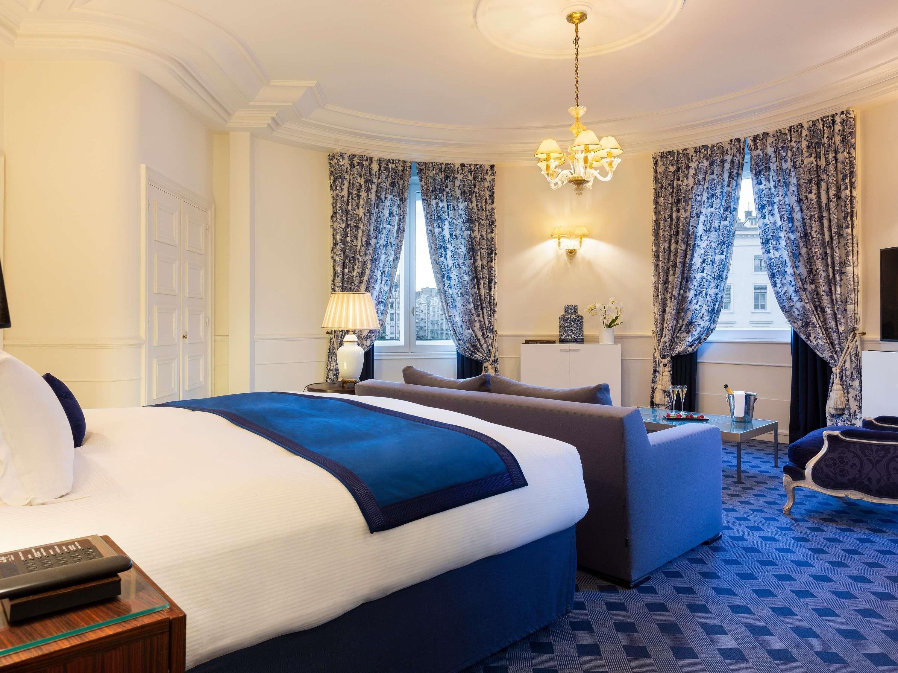 A hotel room with a large bed, a sofa, a desk, and a chandelier.