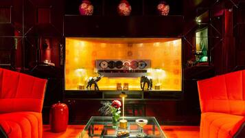 Une pièce avec des fauteuils à revêtement rouge, une table basse en verre ornée d’un vase et d’une boisson, et un mur décoré de vases et d’une platine vinyle.
