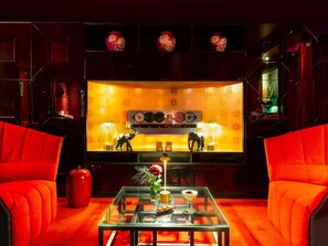 A room with red upholstered chairs, a glass coffee table with a vase and a drink, and a wall with decorative vases and a record player. - Le Royal Hotel Lyon - MGallery Collection (Lyon)