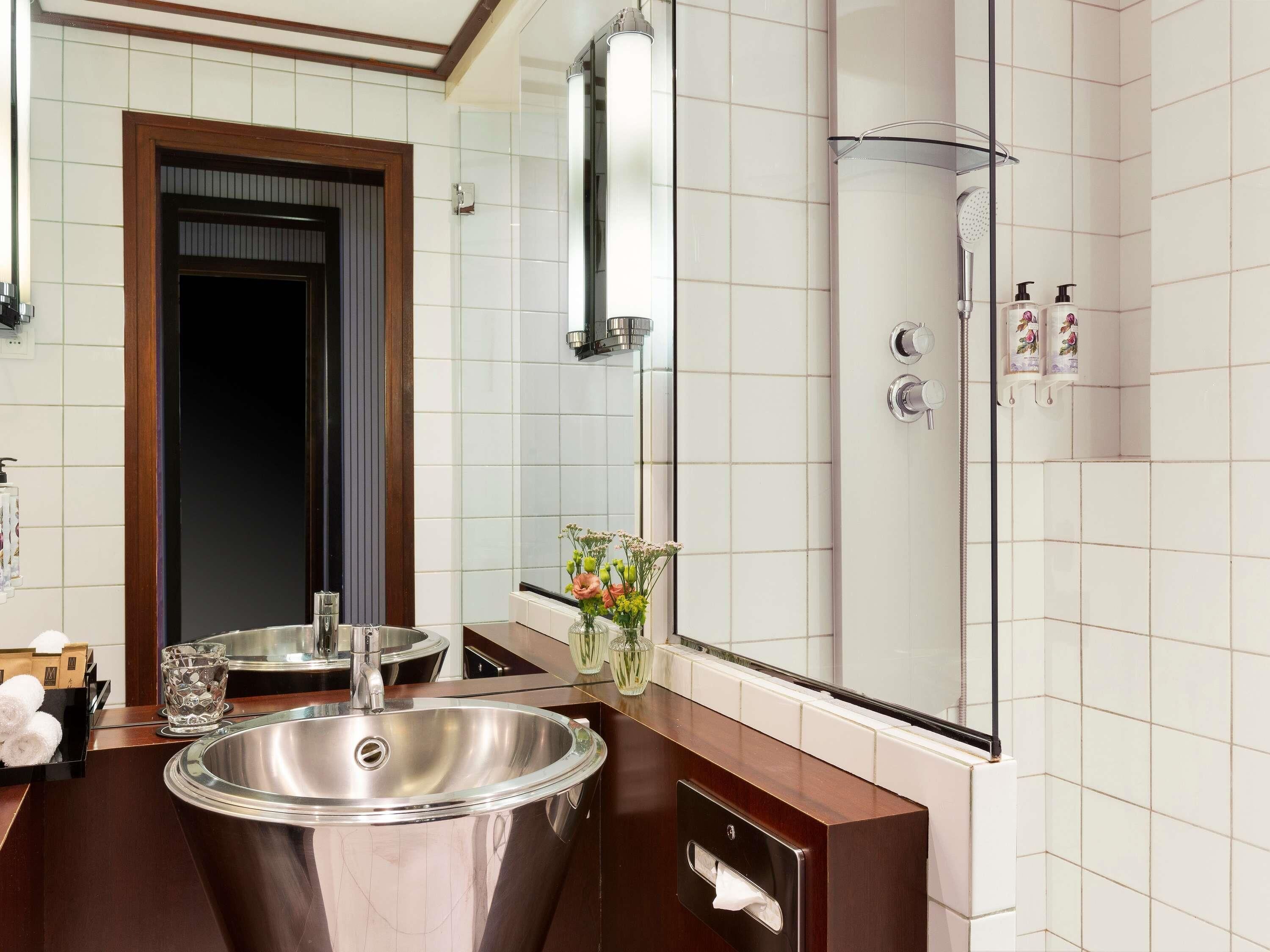 A bathroom with a sink, mirror, shower, and toiletries.