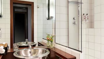 A bathroom with a sink, mirror, shower, and toiletries.