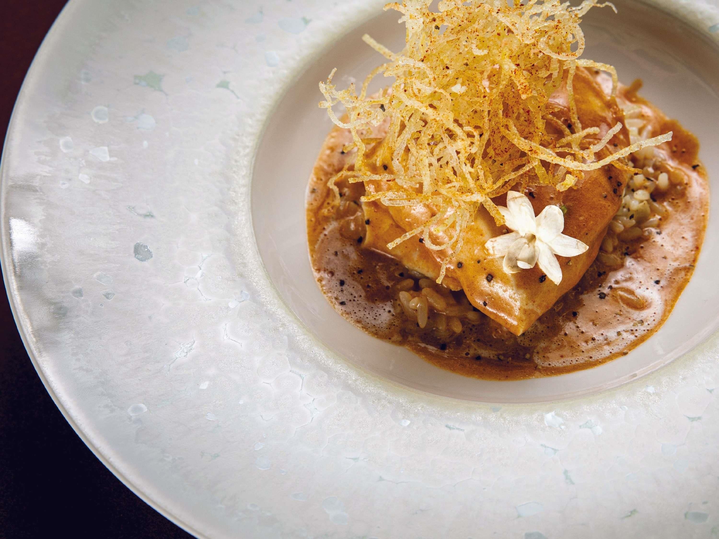 Une assiette contenant un plat, peut-être un dessert, agrémenté d’une garniture râpée et d’une fleur.