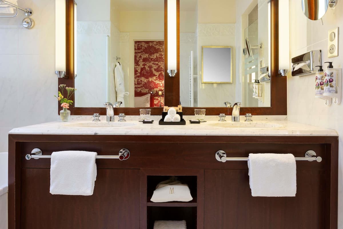 Une salle de bain équipée d’un meuble-lavabo à deux vasques, de deux porte-serviettes, d’un miroir et d’un distributeur de serviettes.