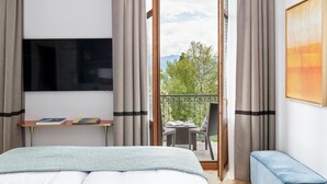 Une chambre à coucher avec un lit, un téléviseur fixé au mur, une petite table avec des livres et un balcon avec une table et des chaises.