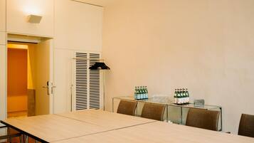 A conference room with a long table, chairs, a glass-top table, and a cabinet with bottles and glasses.