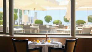 Une table à manger avec des aliments pour le petit-déjeuner, une vue sur les places assises extérieures depuis la fenêtre et des parasols.