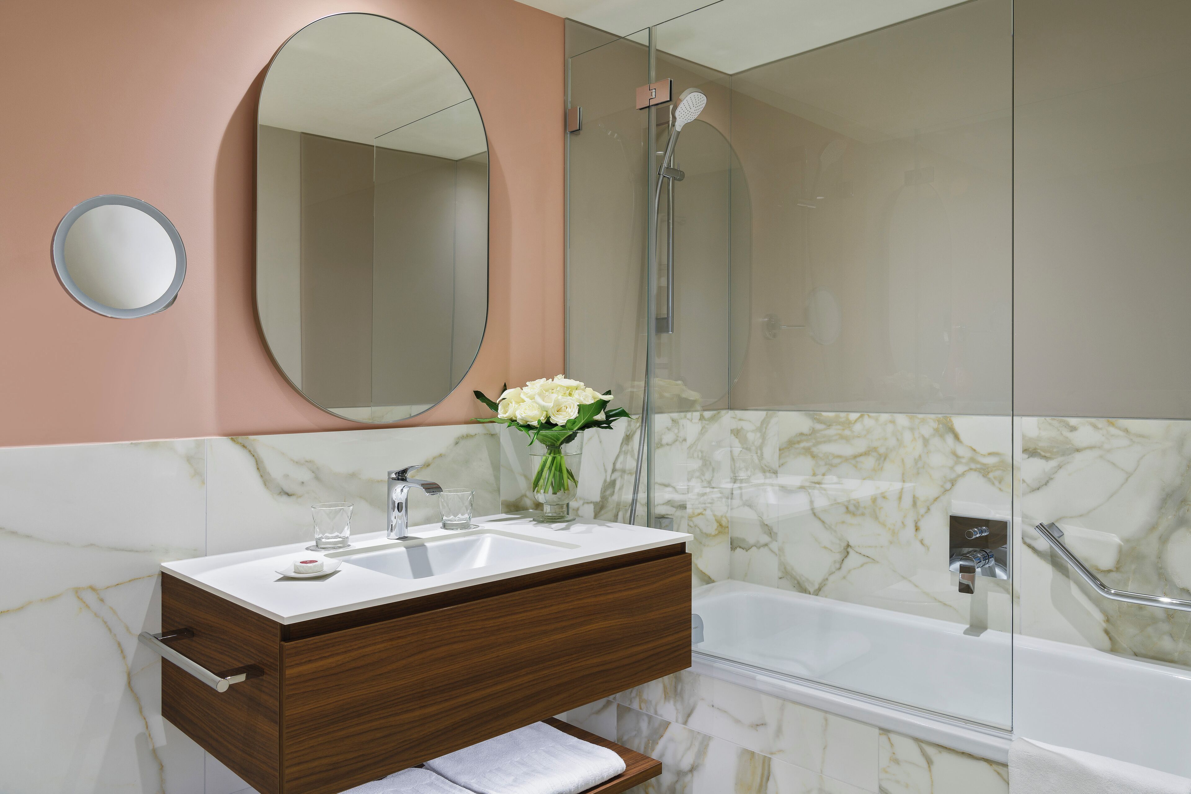 A bathroom with a marble sink, a mirror, a shower, and a towel rack.