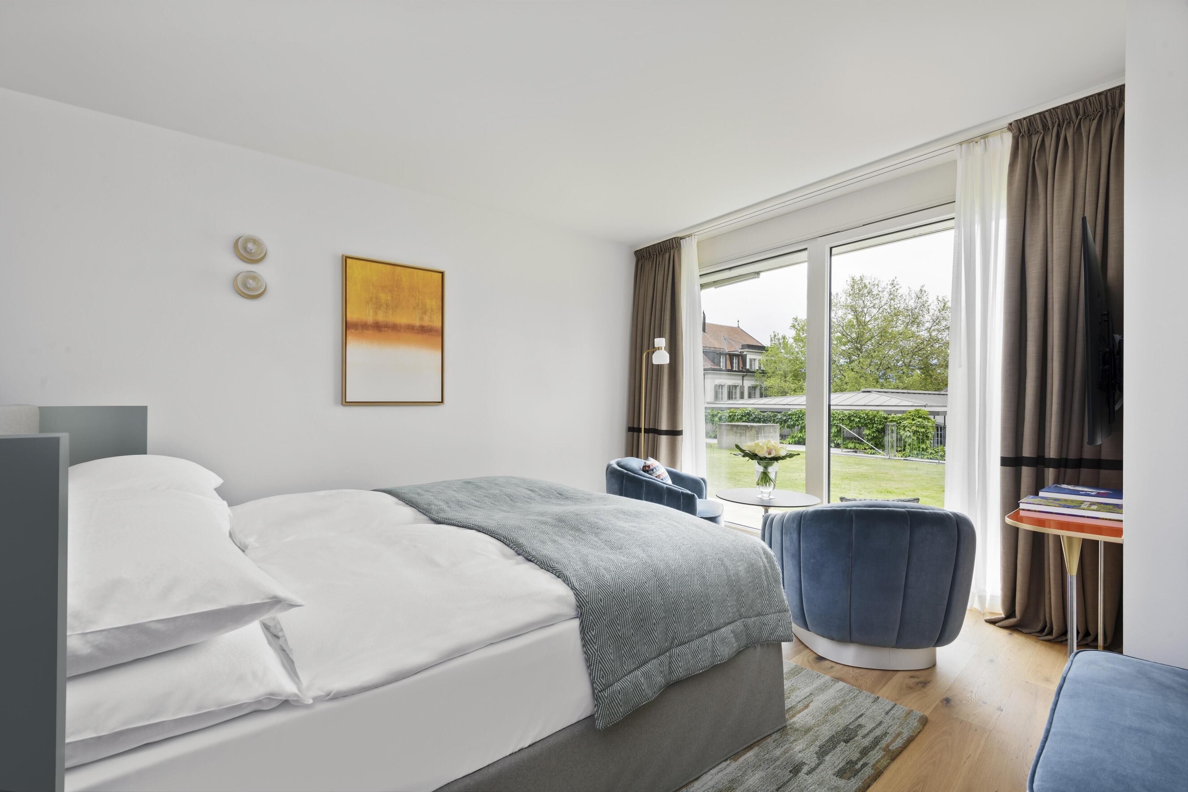 A bedroom with a bed, a chair, a table, a window, and a painting.