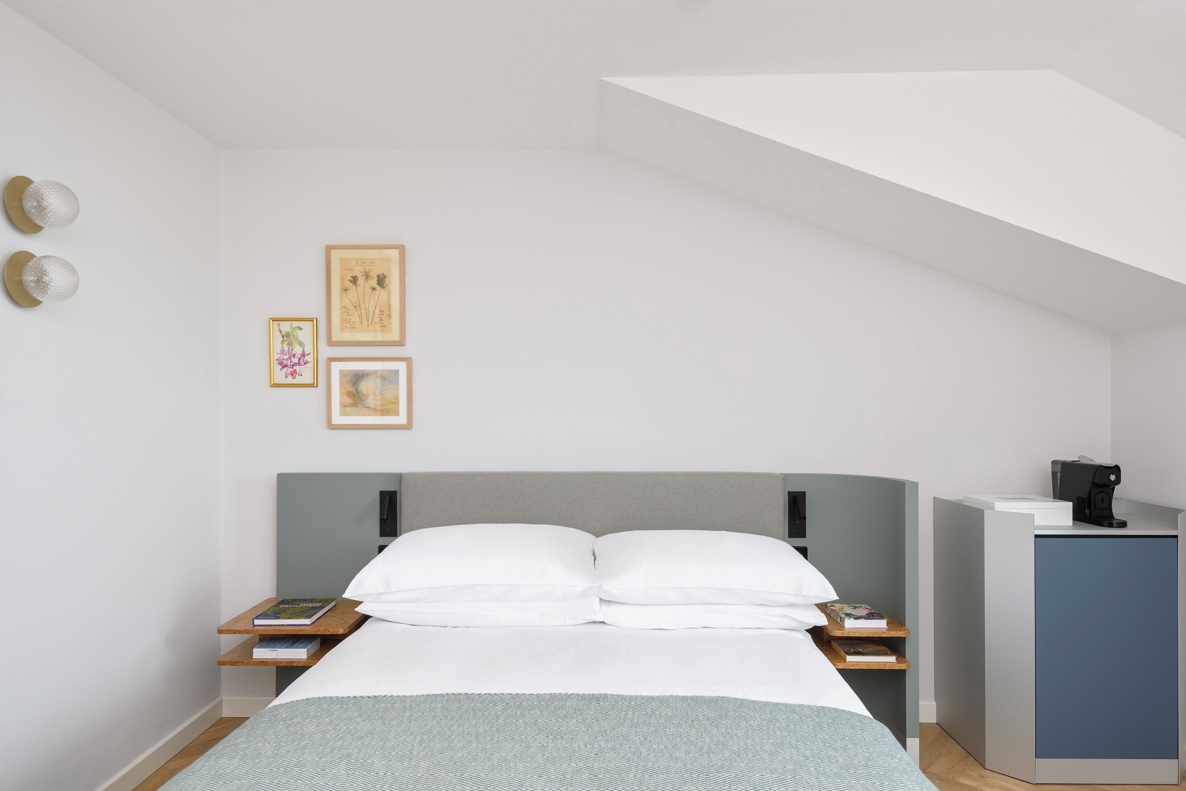 Een moderne slaapkamer met een bed, nachtkastjes, een bureau en afbeeldingen in lijsten aan de muur.