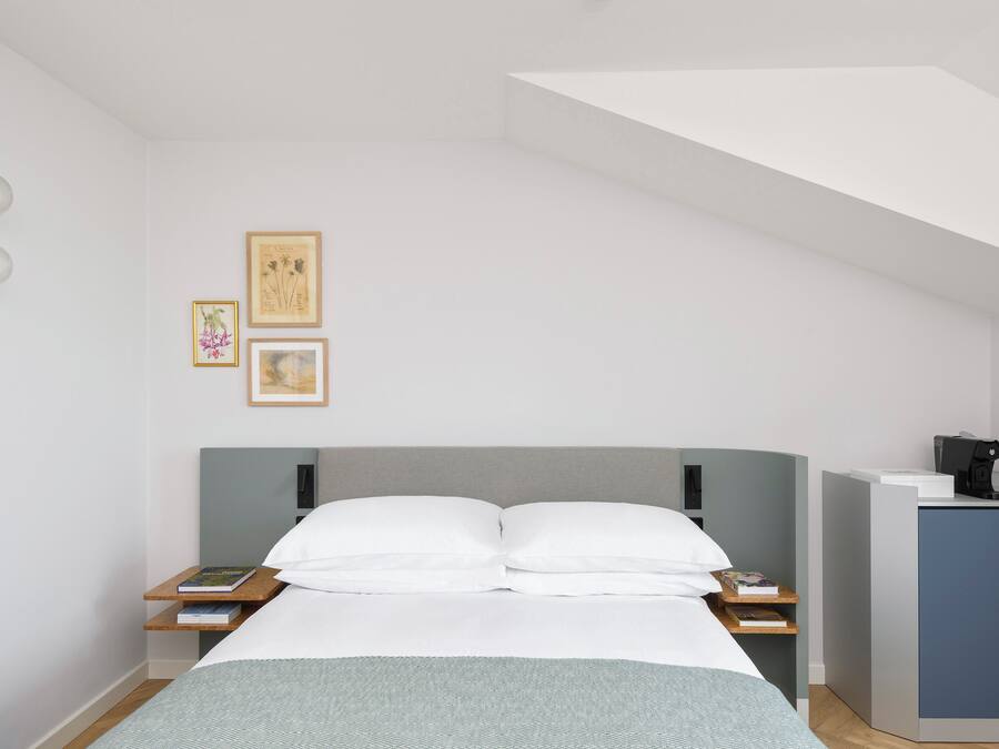 Une chambre à coucher moderne avec un lit, des tables de chevet, un bureau et des tableaux encadrés accrochés au mur.