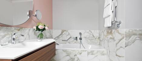 Un baño con pared de mármol, un lavamanos blanco, un espejo, una ducha y un perchero para toallas.