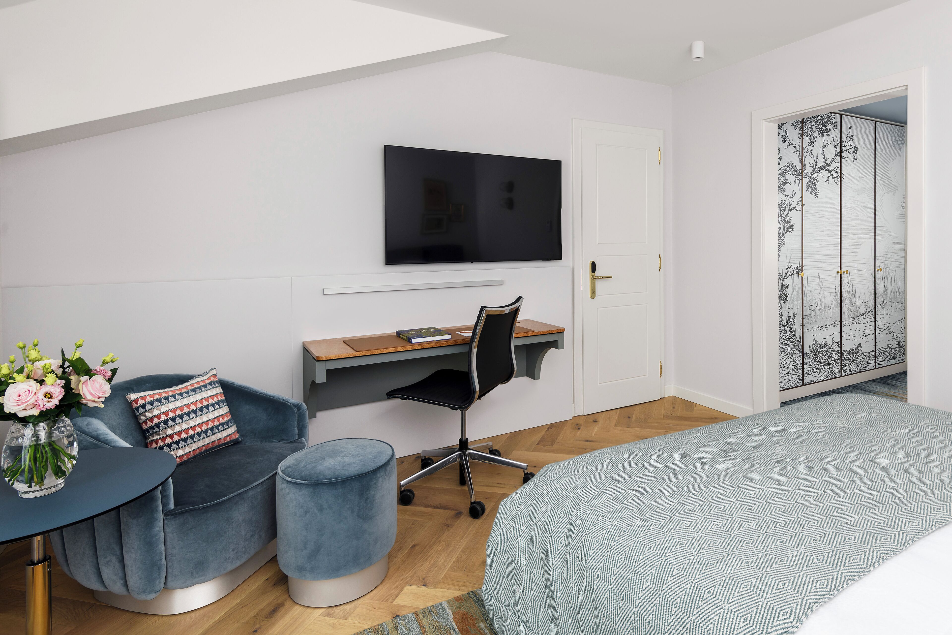 Ein modernes Schlafzimmer mit Bett, Schreibtisch, Stuhl, Fernseher und einer dekorativen Wandverkleidung.
