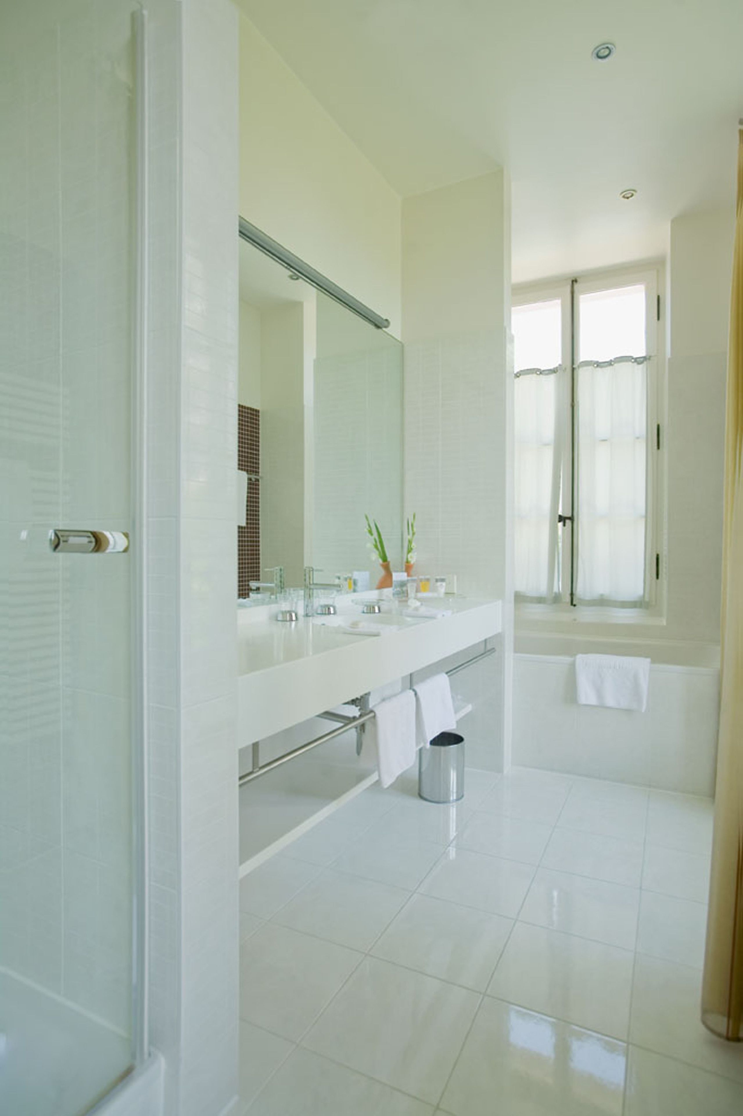 A modern bathroom with a large mirror, two sinks, a shower, and a toilet.