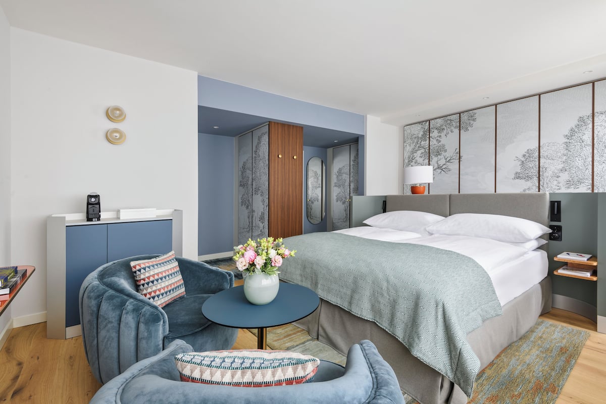 A modern hotel room with a bed, a desk, a chair, and a small table with a vase of flowers.