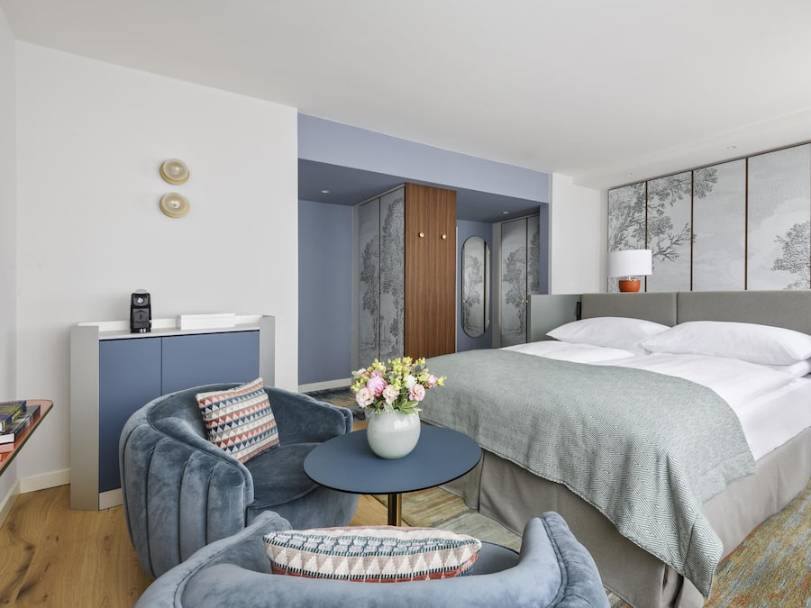 Une chambre d’hôtel moderne, équipée d’un lit, d’un bureau, d’une chaise, d’une petite table agrémentée de fleurs et d’un mur décoré d’œuvres d’art.