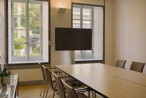Un salón de conferencias con una larga mesa, sillas, una pantalla grande y ventanas que dan a zonas verdes.