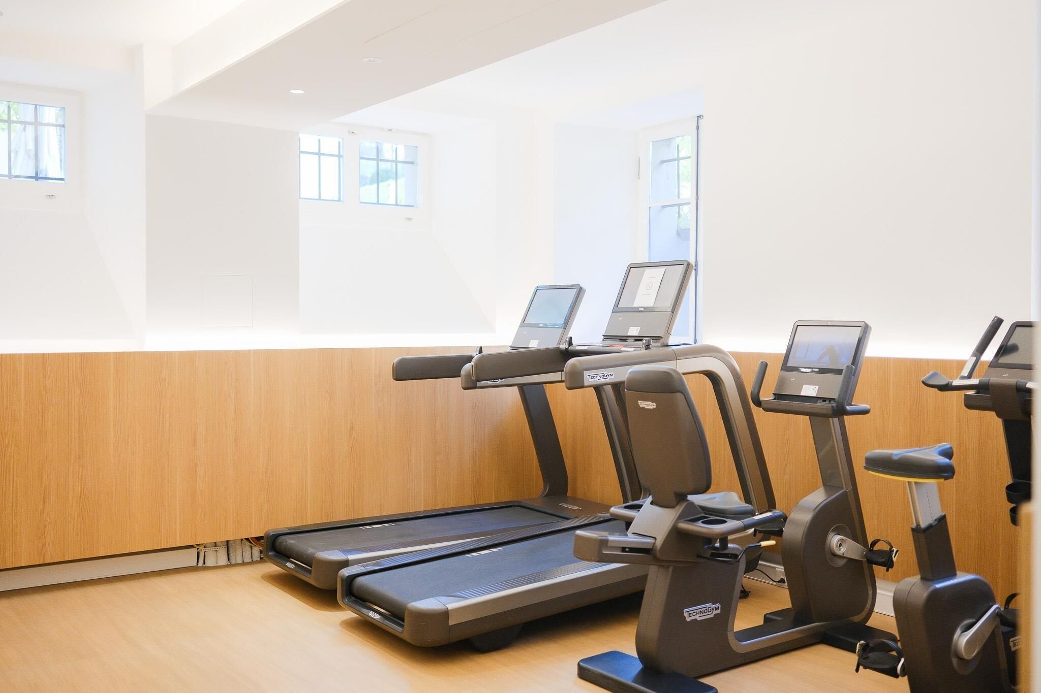 Un gimnasio con cintas de correr y elípticas, paneles de madera y ventanas amplias.