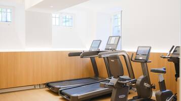 Un gimnasio con cintas de correr y elípticas, paneles de madera y ventanas amplias.