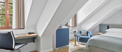 A modern bedroom with a sloped ceiling, a desk, a chair, a bed, and a small table with a vase of flowers.