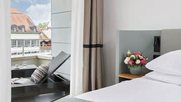Quarto de hotel com cama, uma pequena mesa com um vaso de flores e vista para edifícios.