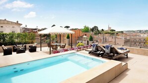 A rooftop pool with lounge chairs and a table, surrounded by flowers and a pergola. - Sina Bernini Bristol, Autograph Collection (Rome)