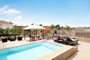 Una piscina sul tetto con poltrona a sdraio e tavolo, circondata da fiori e un pergolato.