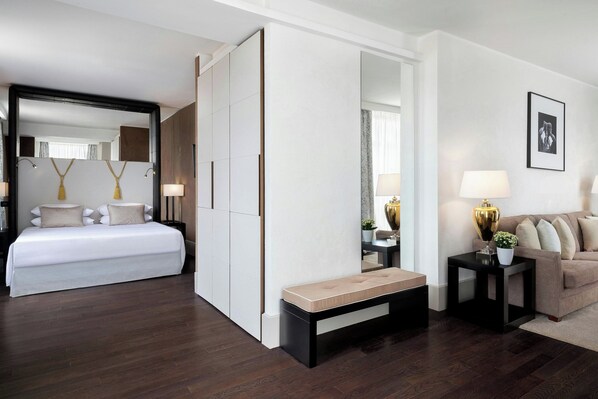A modern hotel room with a large bed, a bench, a sofa, and a small table with a lamp. - Sina Bernini Bristol, Autograph Collection (Rome)