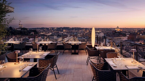An outdoor dining area with tables and chairs, overlooking a cityscape at sunset. - Sina Bernini Bristol, Autograph Collection (Rome)