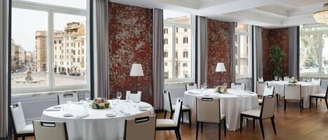 A restaurant with round tables set for dining, large windows with city views, and elegant chandeliers.