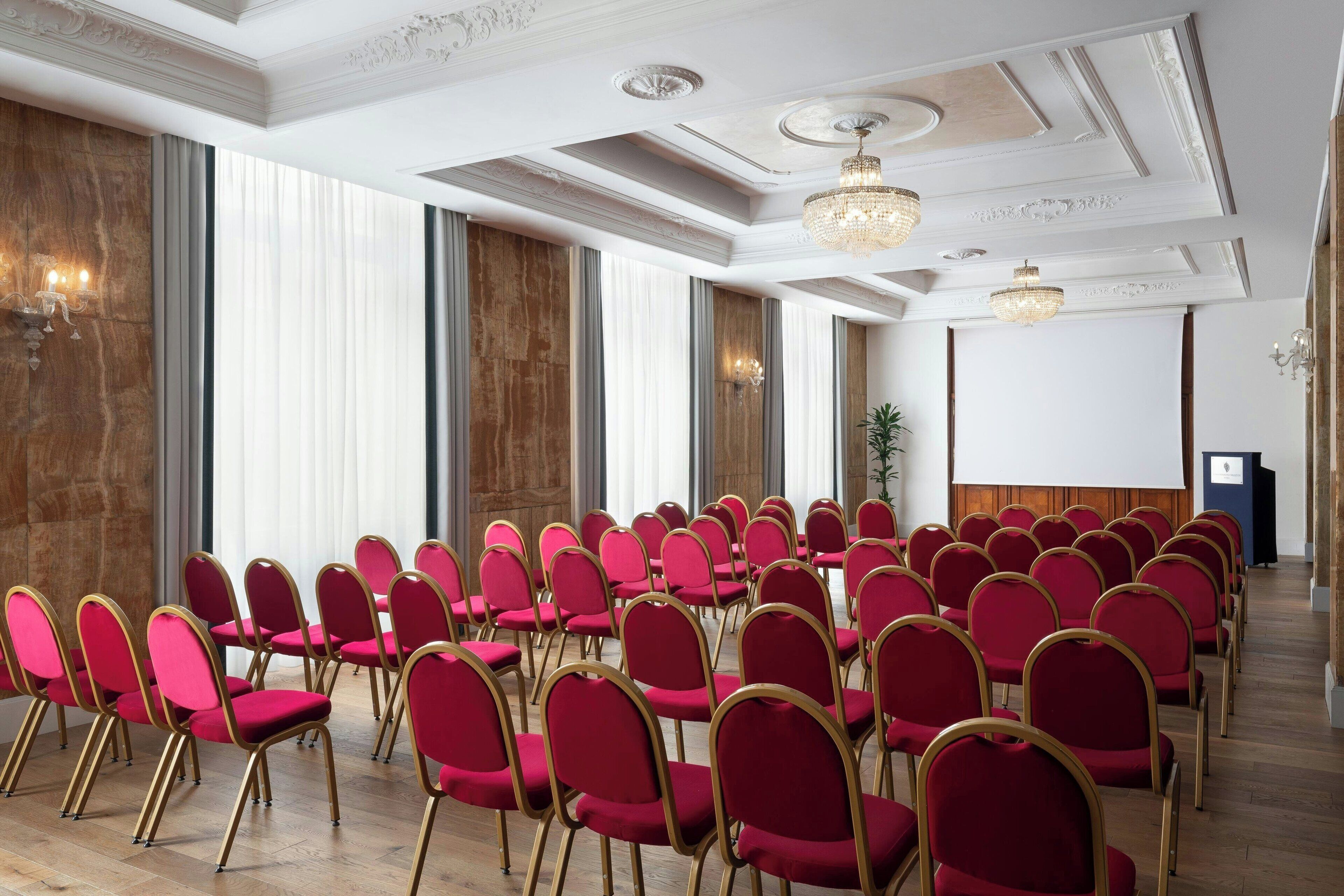 A conference room with rows of red chairs and a large screen at the front.