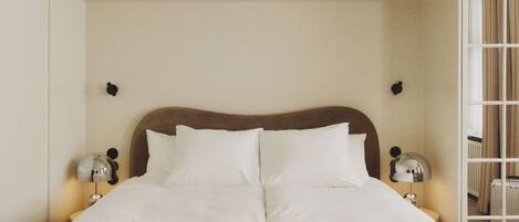 A neatly made bed with white linens, two bedside lamps, and a view of a window with curtains.