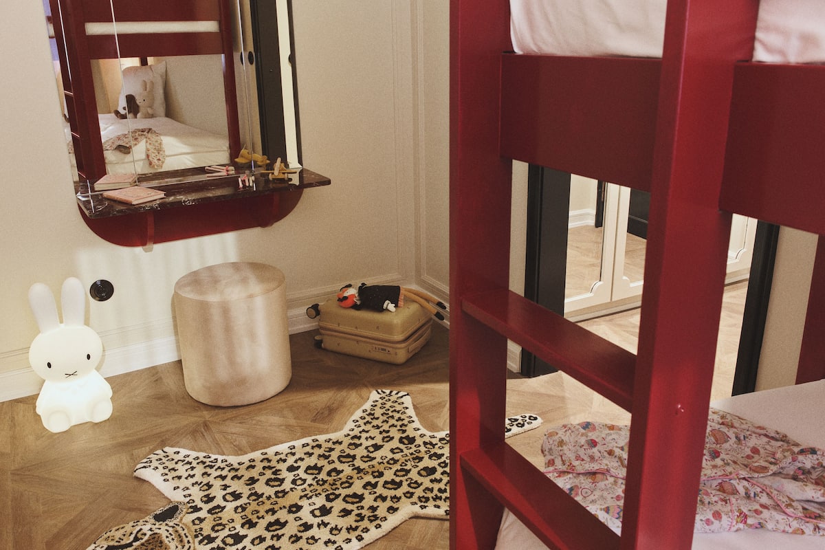 A child's room with a bunk bed, a mirror, a small stool, a toy rabbit, a suitcase, and a leopard print rug.