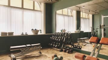 Uma academia com equipamentos de exercício, um banco e um espelho.
