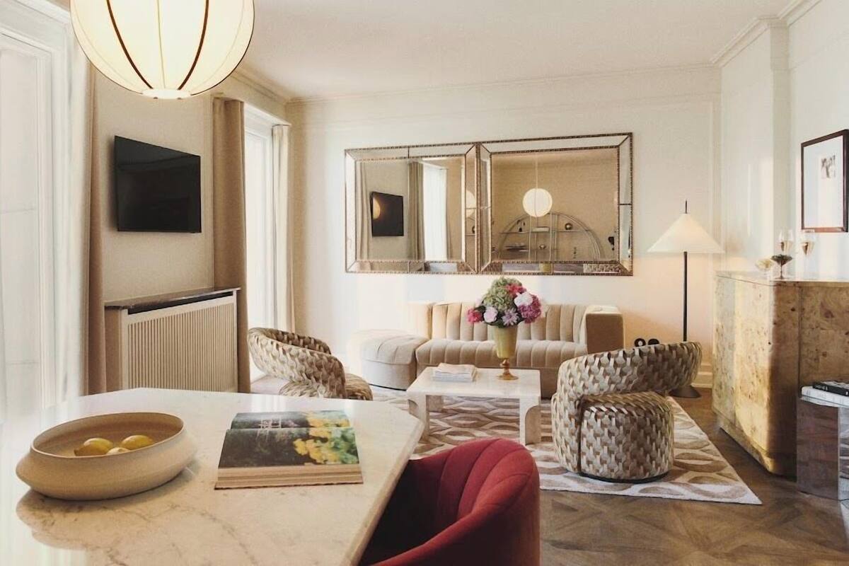 A modern living room with a marble table, red chairs, a sofa, and a large mirror.