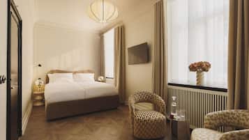 Een hotelkamer met een groot bed, een fauteuil, een bijzettafeltje met glazen, een vaas met bloemen en een televisie aan de muur.