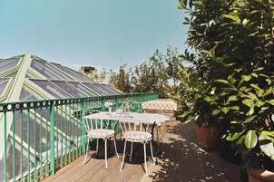 A greenhouse with a glass roof, wooden deck, and white metal chairs.