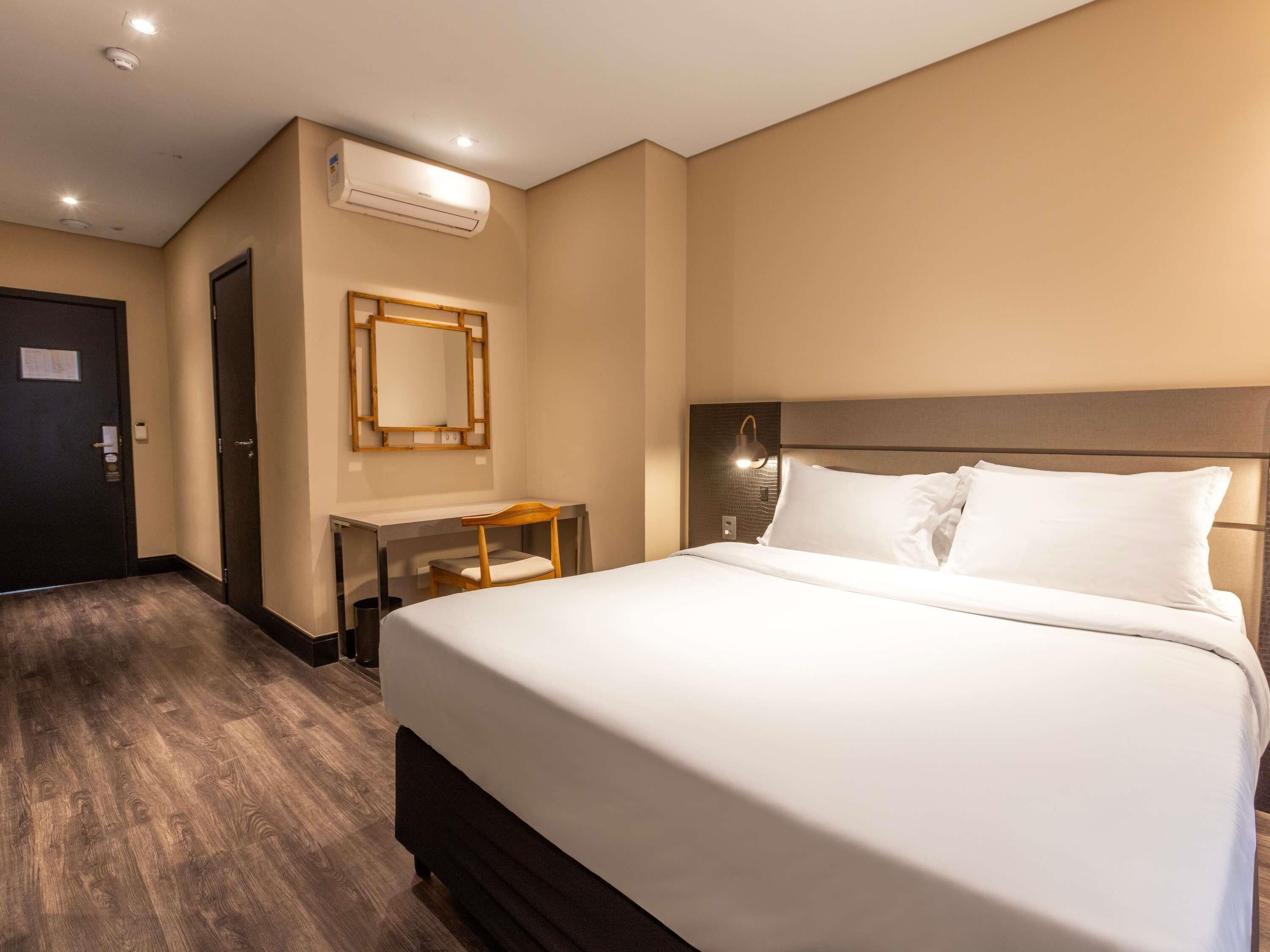 Una habitación de hotel con una cama grande, un escritorio, un espejo y un equipo de aire acondicionado.