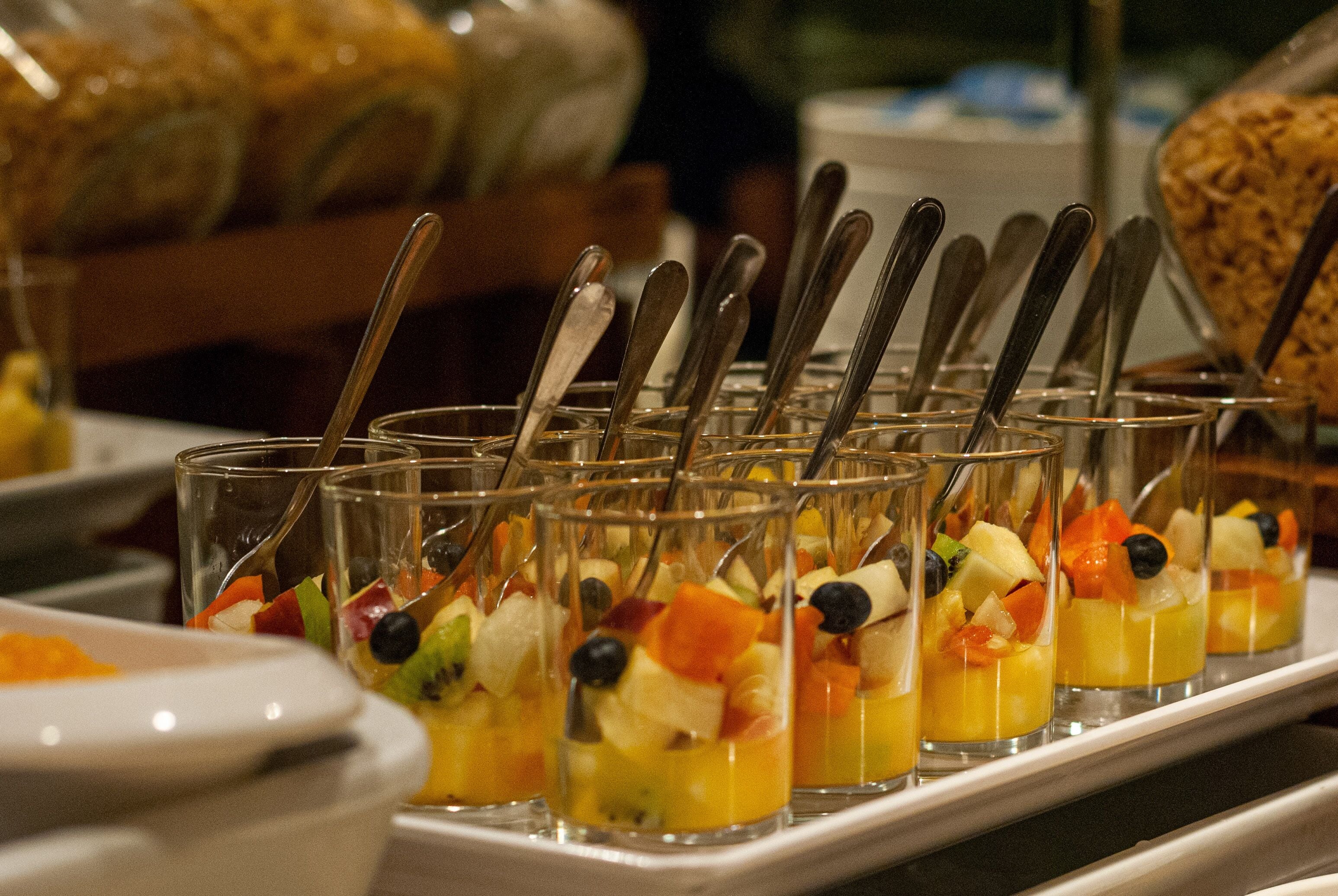 A buffet with fruit parfaits in glasses and spoons.