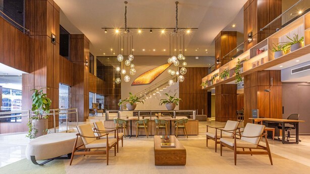 Un hall espacioso con una zona de estar central, paneles de madera y lámparas esféricas colgantes.
