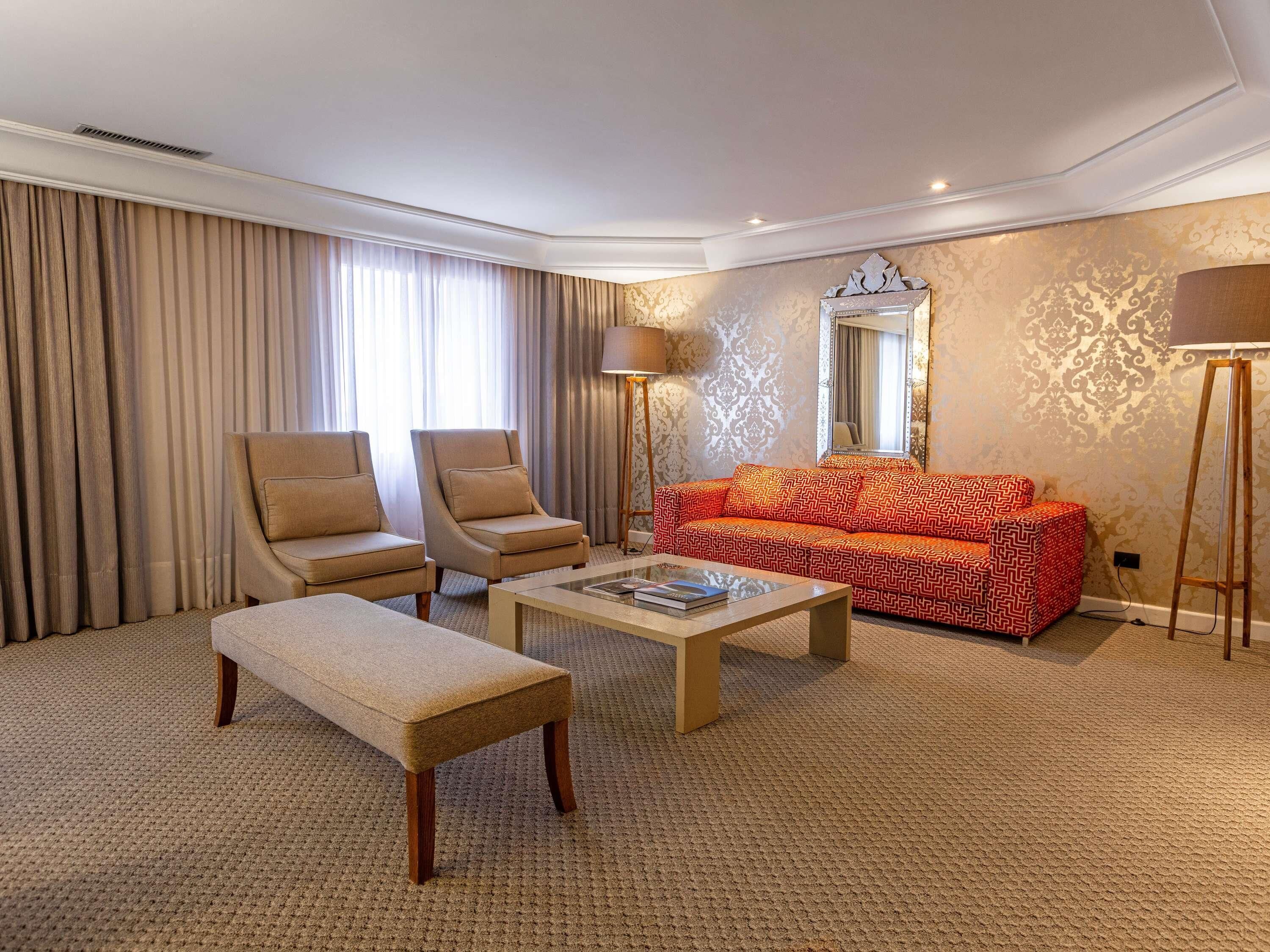 A hotel room with a sofa, two armchairs, a coffee table, a lamp, and a mirror.