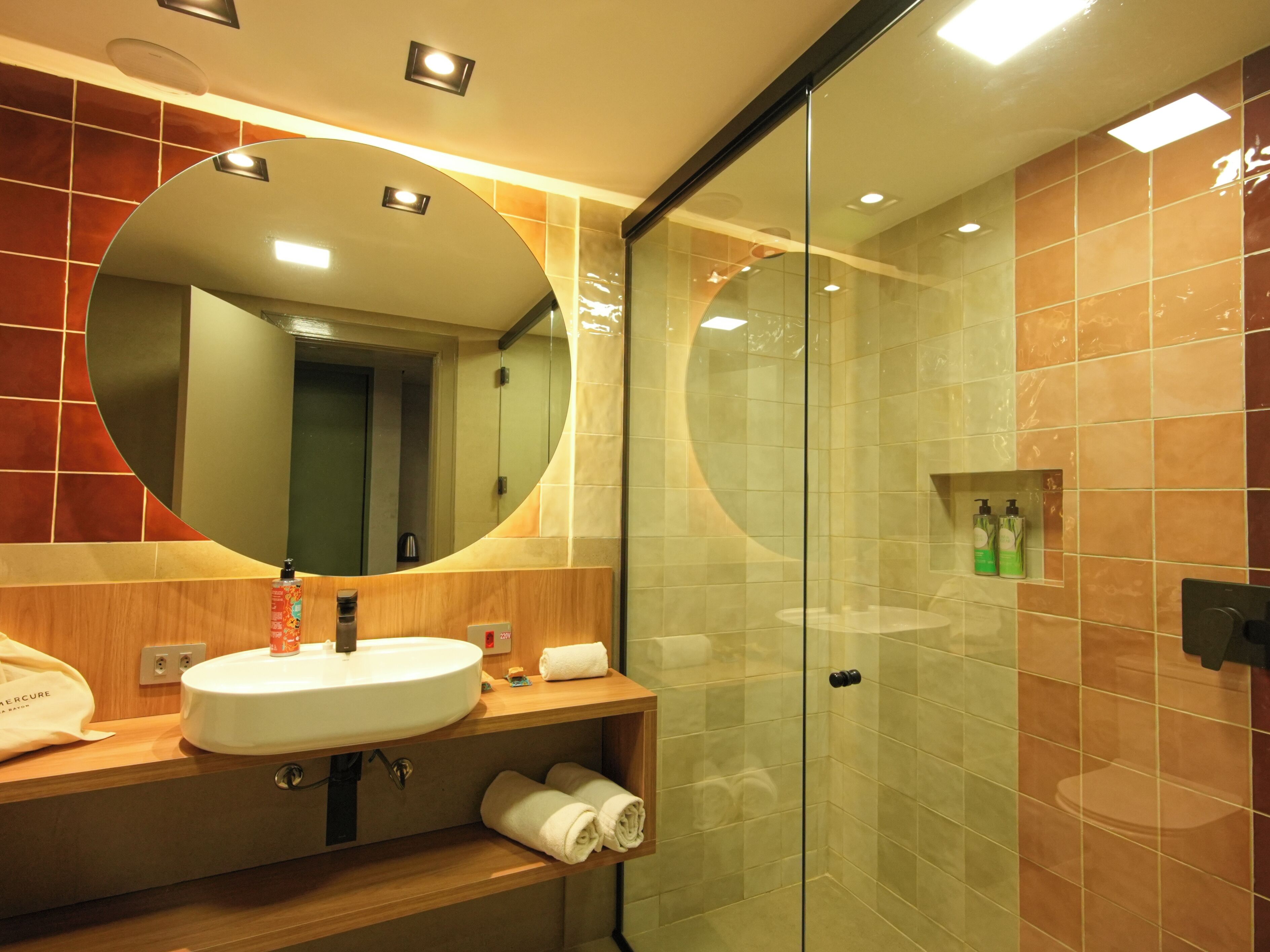 Un baño moderno con un espejo redondo, un lavabo y una cabina de ducha de vidrio.