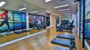 Un gimnasio con equipo de ejercicio, un espejo grande y piso de madera.