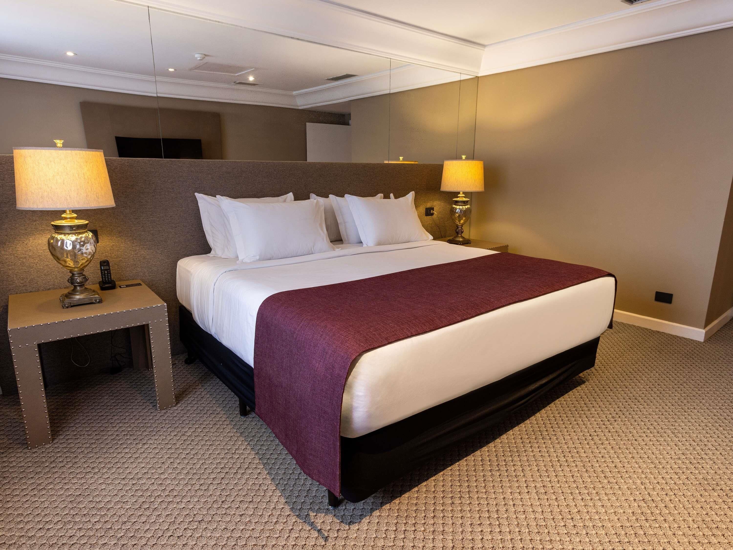 A hotel room with a large bed, two bedside lamps, a nightstand, and a carpeted floor.