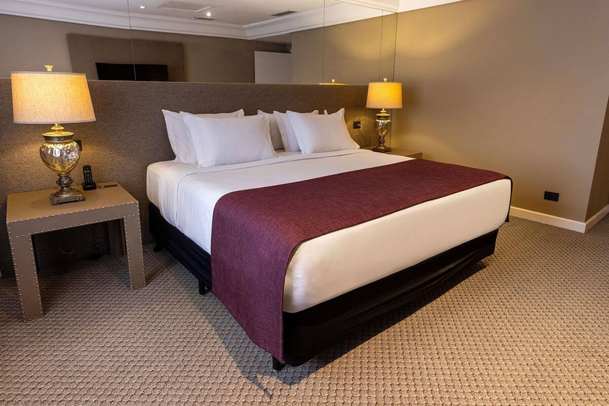 A hotel room with a large bed, two bedside lamps, a nightstand, and a carpeted floor.