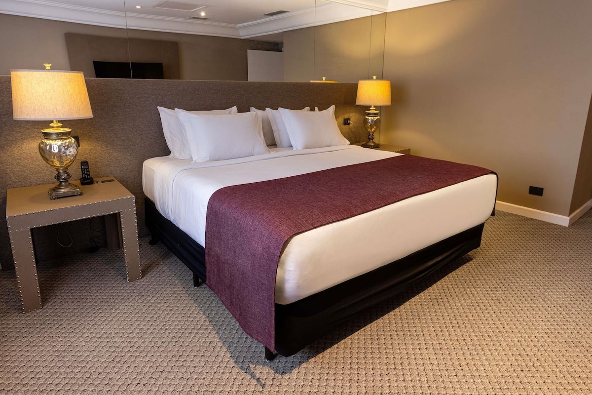 A hotel room with a large bed, two bedside lamps, a nightstand, and a carpeted floor.