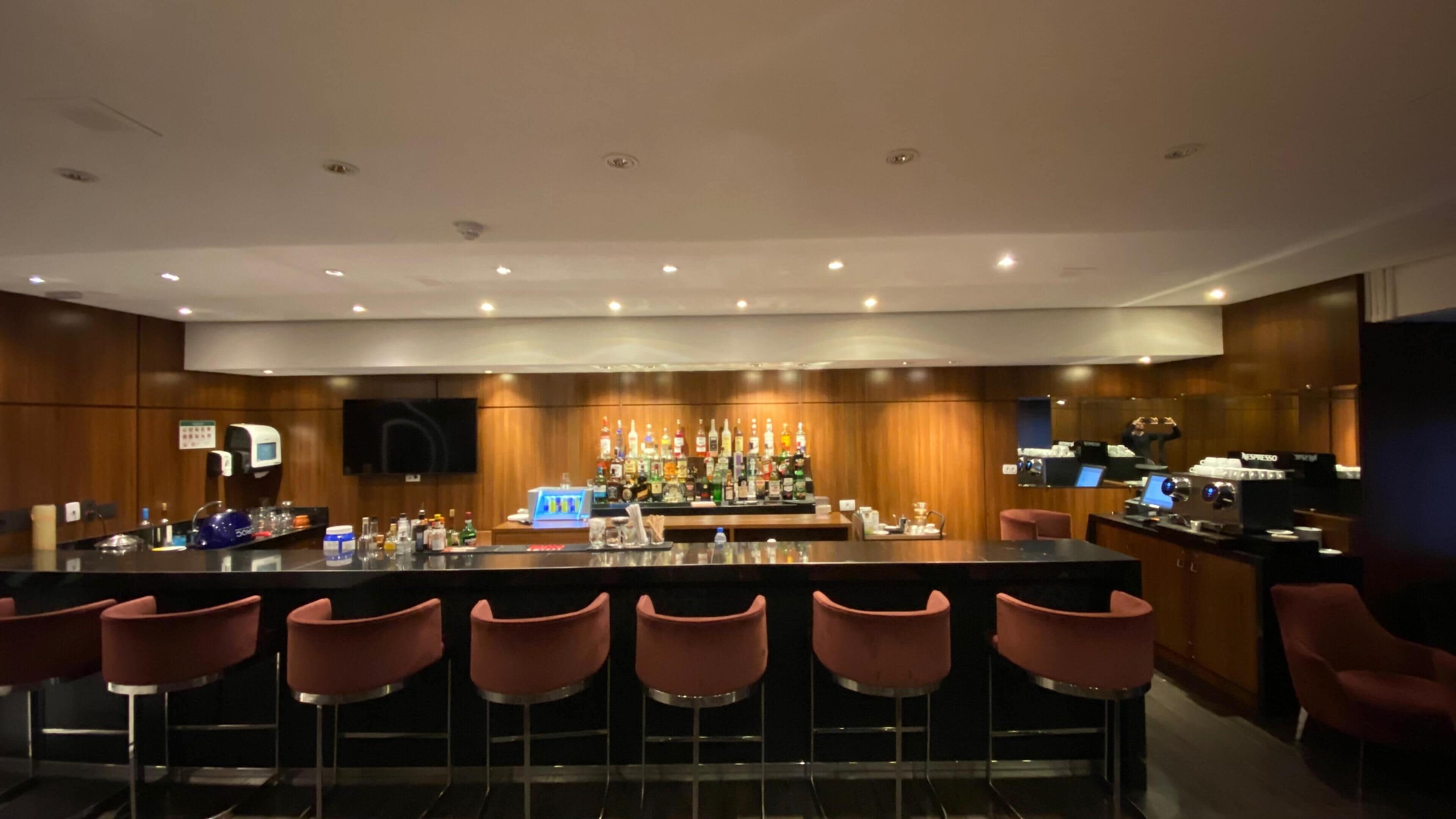 Zona de bar moderna con una barra larga, varios taburetes y una selección de botellas de licor.