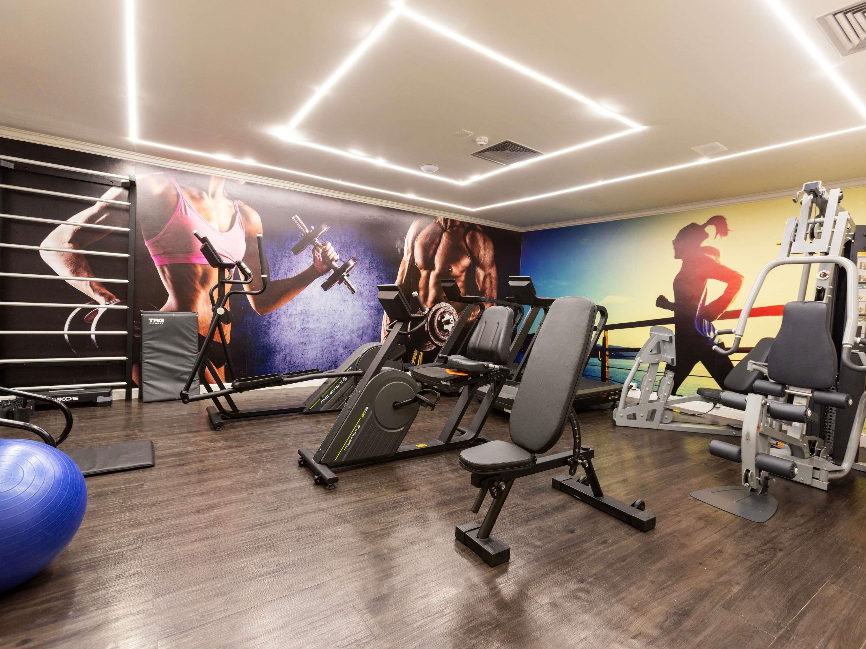 Ein Fitnessstudio mit Trainingsgeräten, einem blauen Übungsball und einer Wand mit Wandbildern zum Thema Fitness.