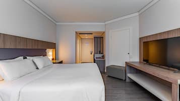 Habitación de hotel con una cama grande, televisión, escritorio y baño visible a través de una puerta abierta.