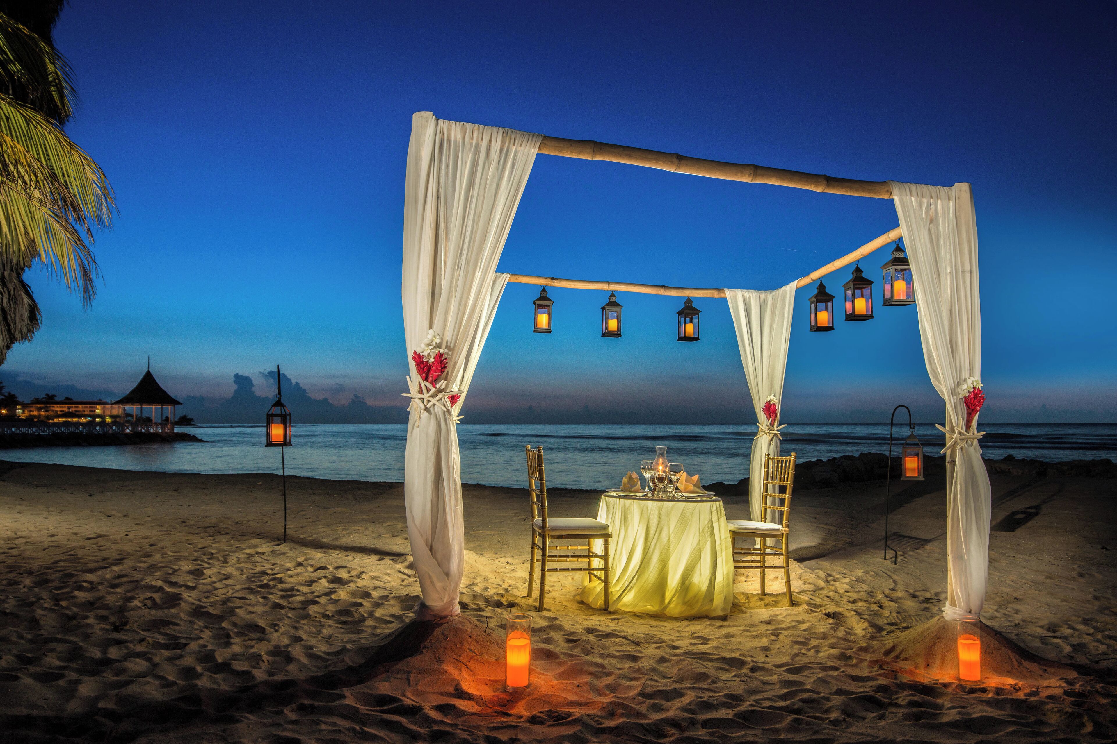 A beach wedding setup with a canopy, chairs, a table, and lanterns.