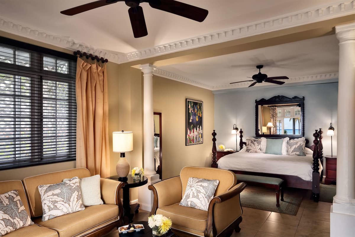 Une chambre d’hôtel comprenant un lit, un canapé, une chaise, une petite table avec une lampe et une fenêtre avec des stores.